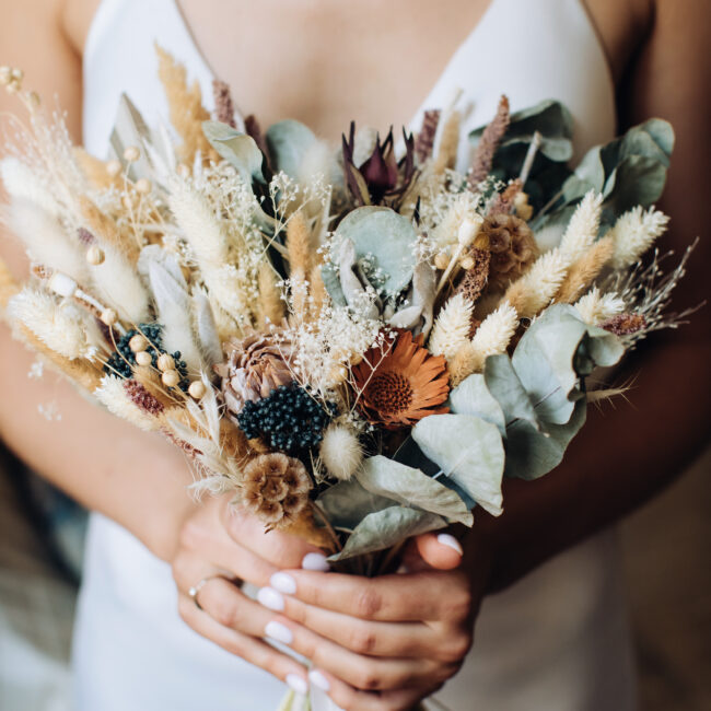 The bride holds in her hands an elegant bouquet of wildflowers in the style of boho. Wedding trends